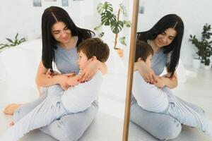 heiter Mutter Sitzung auf Couch im gemütlich Licht Leben Zimmer hält auf Runde kitzelt von wenig Sohn genießen komisch Aktivitäten auf Wochenende beim heim, haben Spaß zusammen, unbezahlbar Zeit mit Vorschule Kind Konzept foto