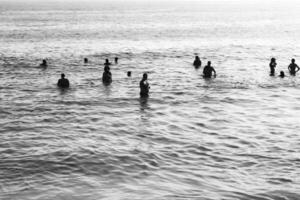 schwarz und Weiß fotografieren von ein Gruppe von Menschen im das Wasser beim das Strand foto