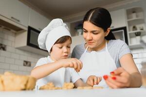 wenig Junge Portion seine Mutter mit das Backen im das Küche Stehen beim das Zähler neben ihr kneten das Teig zum das Kuchen foto