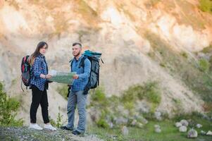 Paar im Liebe Reisen im das Berge mit ein Karte und Fernglas. freunde Reisende sind suchen zum Richtungen auf das Karte. Mann und Frau Touristen im das Berge. springen und jubeln Das Sie haben foto