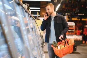 jung Mann Kauf Lebensmittel beim das Supermarkt. andere Kunden im Hintergrund. Konsumismus Konzept. foto