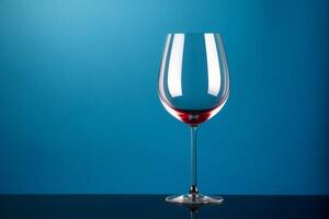 ai generiert ein Single isoliert Wein Glas auf ein Blau Oberfläche mit ein wenige Tropfen von rot Wein Innerhalb reflektieren das Umfeld und Hintergrund. Kopieren Raum. foto