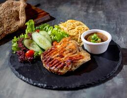 gegrillt ohne Knochen Hähnchen Steak mit Chili Soße, Salat, Nudeln im ein Gericht Seite Aussicht auf dunkel Hintergrund foto