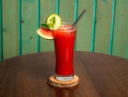 ein Glas von Wassermelone Saft Shake mit roh Wassermelone, Limette und Stroh isoliert auf hölzern Tabelle Seite Aussicht gesund trinken zum Vitamin c foto