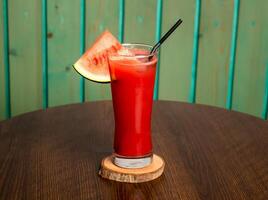 ein Glas von Wassermelone Saft Shake mit roh Wassermelone, Stroh isoliert auf hölzern Tabelle Seite Aussicht gesund trinken zum Vitamin c foto