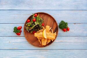 Tal angeschlagen Kabeljau Fisch und Chips mit Salat, Limette und Kirsche Tomate serviert im Gericht isoliert auf hölzern Tabelle oben Aussicht Fast Food foto