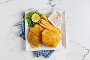 gebraten Fisch und Chips mit Limette im ein Gericht Korb isoliert auf Serviette Seite Aussicht auf grau Hintergrund berühmt indisch und pakistanisch Essen foto