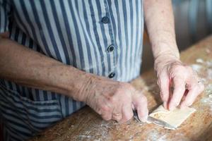Typisches asturisches Weihnachtsdessert, Casadielles. Die Hände einer gealterten Frau legen die Füllung aus Nüssen auf den hausgemachten Teig und schneiden ihn mit einem Messer. Gastronomie foto