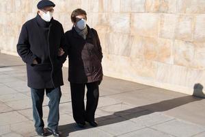 älteres paar über 70, das mit lässigen kleidung und masken auf der straße spaziert. Konzept soziale Distanz covid. sonniger Tag. foto