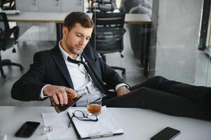 ermüden jung Geschäftsmann Sitzung beim Arbeitsplatz und halten Whiskey Flasche, Trinken Alkohol, Konkurs Konzept. foto