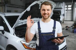 Auto Mechaniker mit Digital Tablette mit Bedienung und Instandhaltung App auf Bildschirm während inspizieren Fahrzeug im Auto Reparatur Geschäft foto