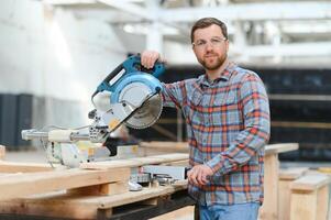 Holz Schneiden Tabelle mit elektrisch kreisförmig gesehen. Fachmann Zimmermann im Uniform Schneiden hölzern Tafel beim Sägewerk Zimmerei Herstellung . Sägen Maschine foto