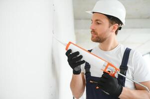 Fachmann Arbeiter bewirbt sich Silikon Dichtmittel mit abdichten Gewehr auf das Mauer foto