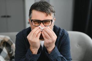 alt Mann erhalten ein kalt und niesen mit Gewebe Papier beim Zuhause foto