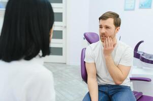 traurig Mann Sitzung im Dental Stuhl Leiden von akut Zahn Schmerz, Reiben seine Wange, schließen hoch. foto