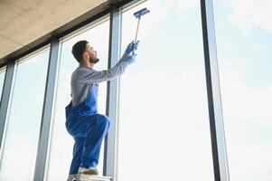 junger mann, der fenster im büro putzt foto