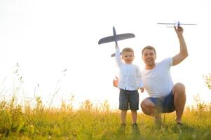 süß wenig Junge und seine gut aussehend jung Papa sind lächelnd während spielen mit ein Spielzeug Flugzeug im das Park. foto