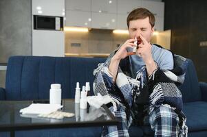krank Mann mit Nasal- sprühen und Papier Gewebe beim Zuhause foto