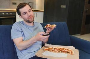 Mann Essen Pizza haben ein wegbringen beim Zuhause entspannend ruhen foto