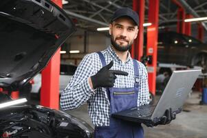 lächelnd Mechaniker mit ein Laptop pc beim das Reparatur Garage. foto