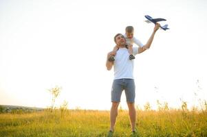 Papa mit seine Sohn beim Sonnenuntergang im Natur. ein Vater Theaterstücke mit Spielzeug Flugzeuge mit seine Sohn beim Sonnenuntergang. Vaters Tag foto
