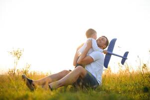 glücklich Vater Kind Moment. Vater Huckepack seine Junge beim Sonnenuntergang während er ist spielen mit Spielzeug Ebene. foto