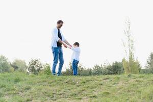 gut aussehend Papa mit seine wenig süß Sohn sind haben Spaß und spielen auf Grün grasig Rasen. glücklich Familie Konzept. Schönheit Natur Szene mit Familie draussen Lebensstil. Familie ruhen zusammen. Väter Tag foto