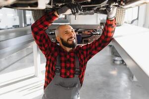 Mechaniker Arbeiten unter Auto beim das Reparatur Garage. Auto Mechaniker Arbeiten im Garage. Reparatur Service. foto