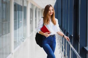 Porträt von ein ziemlich weiblich Schüler mit Bücher und ein Rucksack im das Universität Flur foto