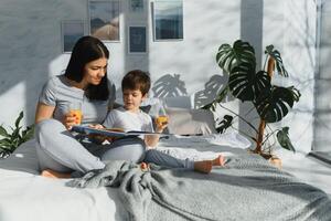 schön Frau mit ihr Sohn Trinken Saft im das Morgen im Bett. gesund Essen Konzept foto