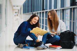 zwei ziemlich weiblich Studenten mit Bücher Sitzung auf das Fußboden im das Universität Flur foto