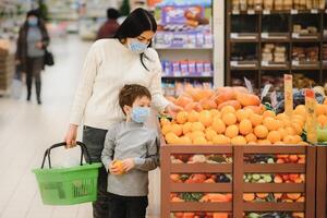 authentisch Schuss von Mutter und Sohn tragen medizinisch Masken zu schützen sich von Krankheit während Einkaufen zum Lebensmittel zusammen im Supermarkt foto