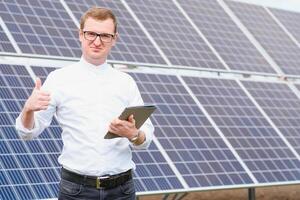 Solar- Energie. jung Geschäft Mann im ein Weiß Hemd in der Nähe von das Solar- Paneele zu Leistung Pflanzen. foto