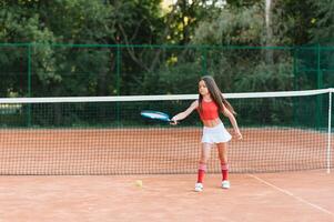 Kind spielen Tennis auf draussen Gericht. wenig Mädchen mit Tennis Schläger und Ball im Sport Verein. aktiv Übung zum Kinder. Sommer- Aktivitäten zum Kinder. Ausbildung zum jung Kind. Kind Lernen zu abspielen foto