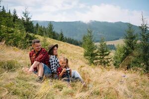 Familie von drei Menschen sich ausruhen im das Berge. Sie saß Nieder zu ausruhen, trinken Wasser nach ein schwer steigen zu das Berg. Sie sind müde aber glücklich. foto