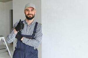 Porträt von gut aussehend Mechaniker mit Stoppel im Blau gesamt, Hemd haben seine Waffen gekreuzt, suchen beim Kamera foto