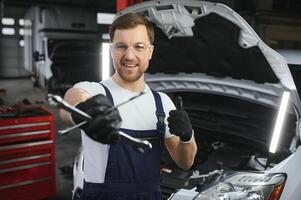 mit Werkzeug im Hand. Erwachsene Mann im farbig Uniform funktioniert im das Automobil Salon foto