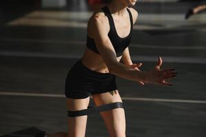 sportlich Mädchen tun Übung zum Gesäß mit Widerstand Band auf grau Hintergrund. Fitness Frau Arbeiten aus foto
