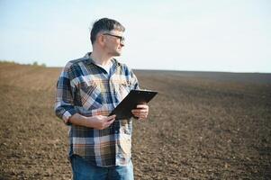 ein Farmer funktioniert im ein Feld gesät im Frühling. ein Agronom Spaziergänge das Erde, beurteilen ein gepflügt Feld im Herbst. Landwirtschaft. Clever Landwirtschaft Technologien. foto