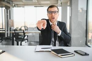 wütend Senior Geschäftsmann Sitzung beim seine Schreibtisch und schreiend foto