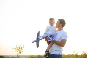 glücklich Vater Kind Moment. Vater Huckepack seine Junge beim Sonnenuntergang während er ist spielen mit Spielzeug Ebene. foto