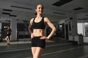 Brünette sexy Fitness-Mädchen in Sportbekleidung mit perfektem Körper im Fitnessstudio posiert vor dem Trainingsset foto