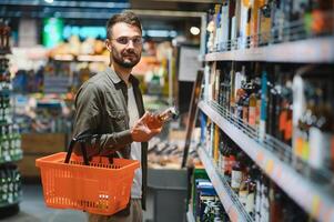 ein Mann nimmt alkoholisch Getränke von das Supermarkt Regal. Einkaufen zum Alkohol im das Geschäft foto