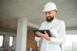 ernst beschäftigt jung attraktiv Arabisch industriell Ingenieur im schwer Hut mit Projekt Zeichnungen im Fabrik Innere. Fachmann und Industrie, Baumeister Architekt Arbeit, Arbeiter Überprüfung Arbeit beim Pflanze Innen- foto