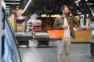 glücklich Mann Kauf gesund Essen und trinken im ein modern Supermarkt und reden auf Telefon. foto