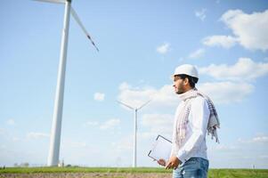 Ingenieur Indien Mann Arbeiten beim Windmühle Bauernhof Erstellen Elektrizität sauber Energie. Wind Turbine Bauernhof Generator durch Alternative Grün Energie. asiatisch Ingenieur Überprüfung Steuerung elektrisch Leistung foto