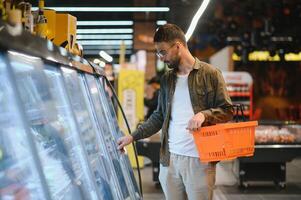 Porträt von lächelnd gut aussehend Mann Lebensmittelgeschäft Einkaufen im Supermarkt, wählen Essen Produkte von Regal foto