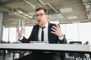 wütend Senior Geschäftsmann Sitzung beim seine Schreibtisch und schreiend foto