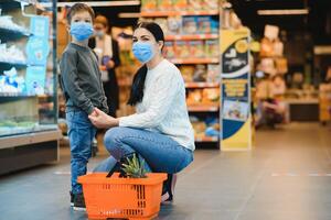 Mutter und ihr Sohn tragen schützend Gesicht Maske Geschäft beim ein Supermarkt während das Coronavirus Epidemie. foto