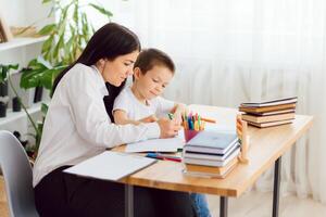 Porträt des hübschen Jungen am Arbeitsplatz mit seinem Tutor, der in der Nähe sitzt und etwas erzählt foto